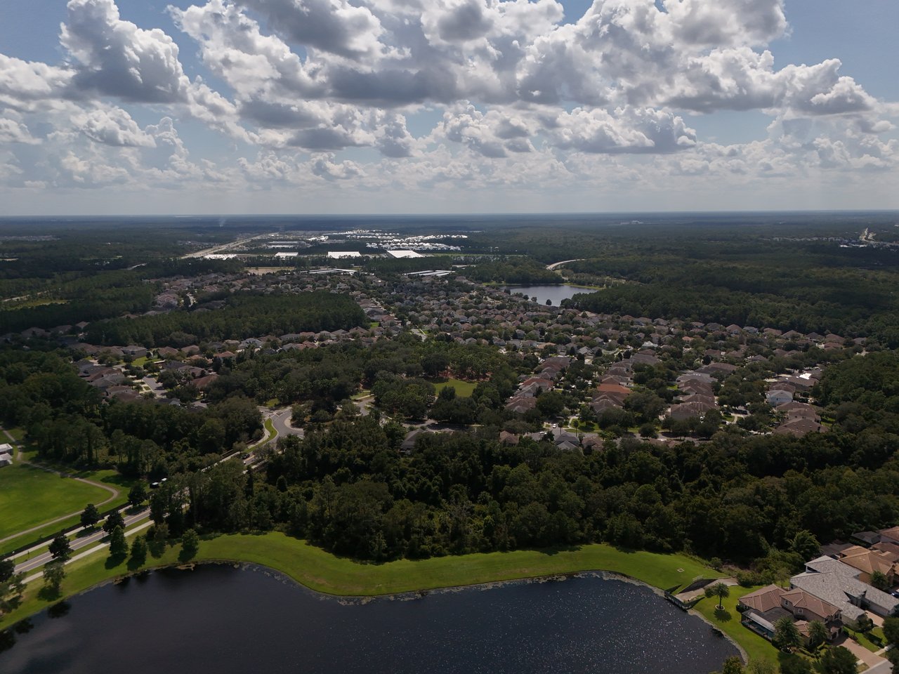 Aerial view of a residential neighborhood beside a lake, with wooded areas and a dramatic cloudy sky.