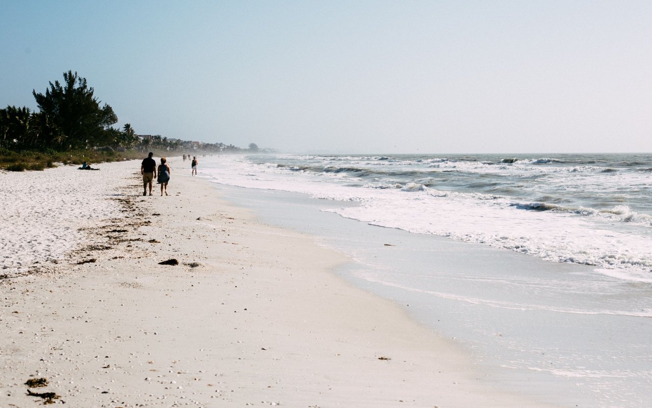 People walk along a sandy beach beside rolling surf.