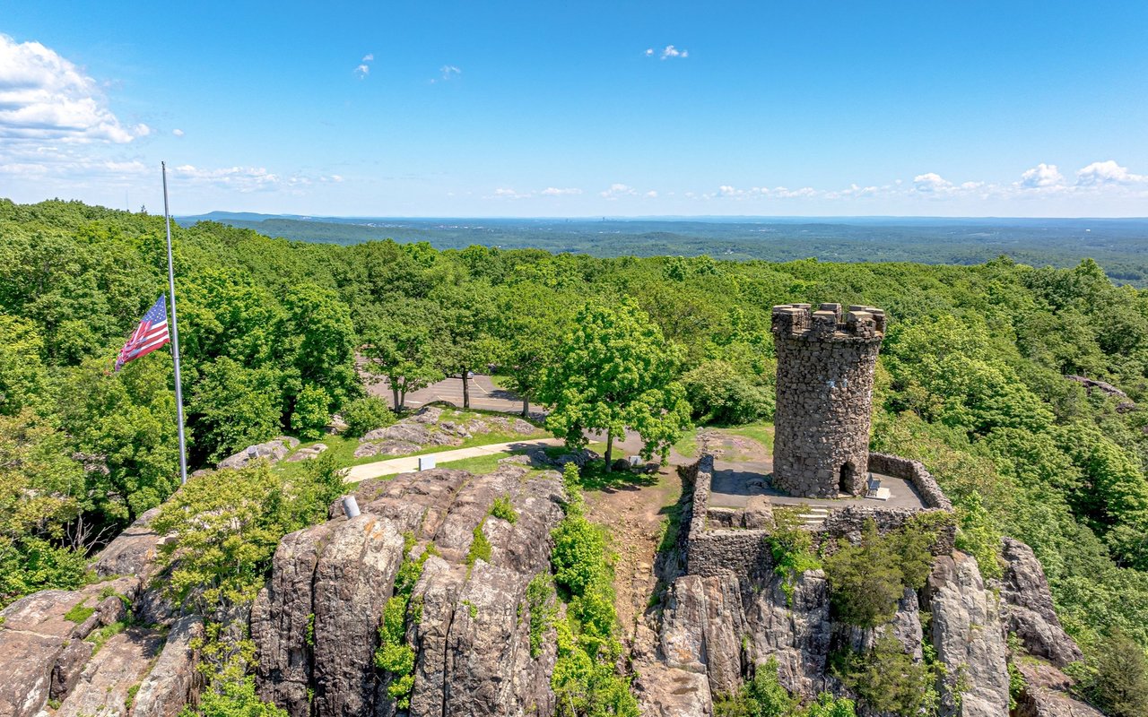 Stone observation tower and American flag overlook wooded hills from a rocky summit in Meriden.