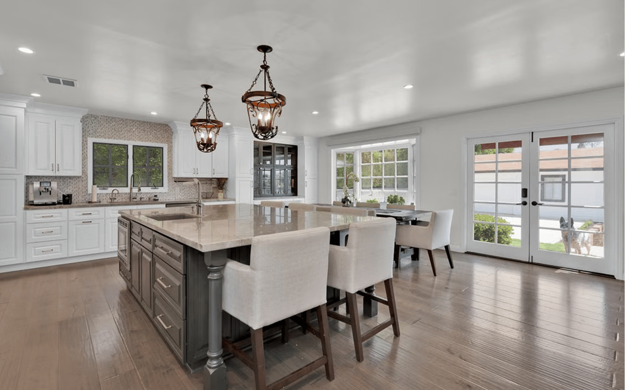 Bright kitchen with a gray island, white cabinetry, pendant lights, and an adjoining dining area.