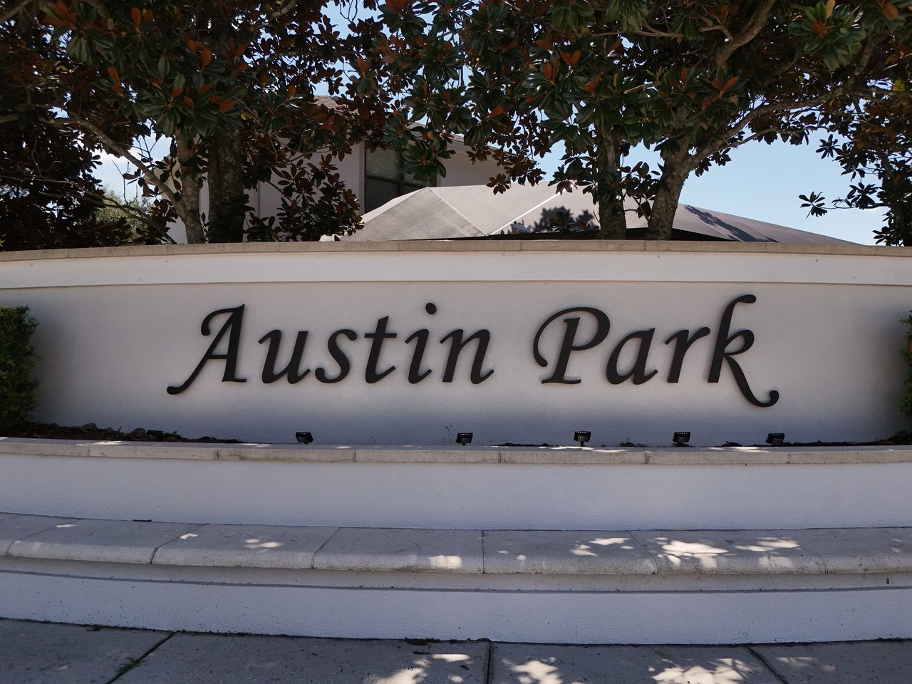 Austin Park entrance sign on a white stucco wall beneath leafy trees.