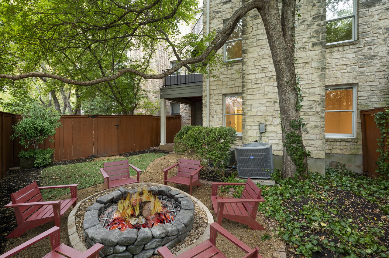 Fenced backyard with stone fire pit under mature trees, virtually staged fire, Winners Circle, Westlake, Austin.