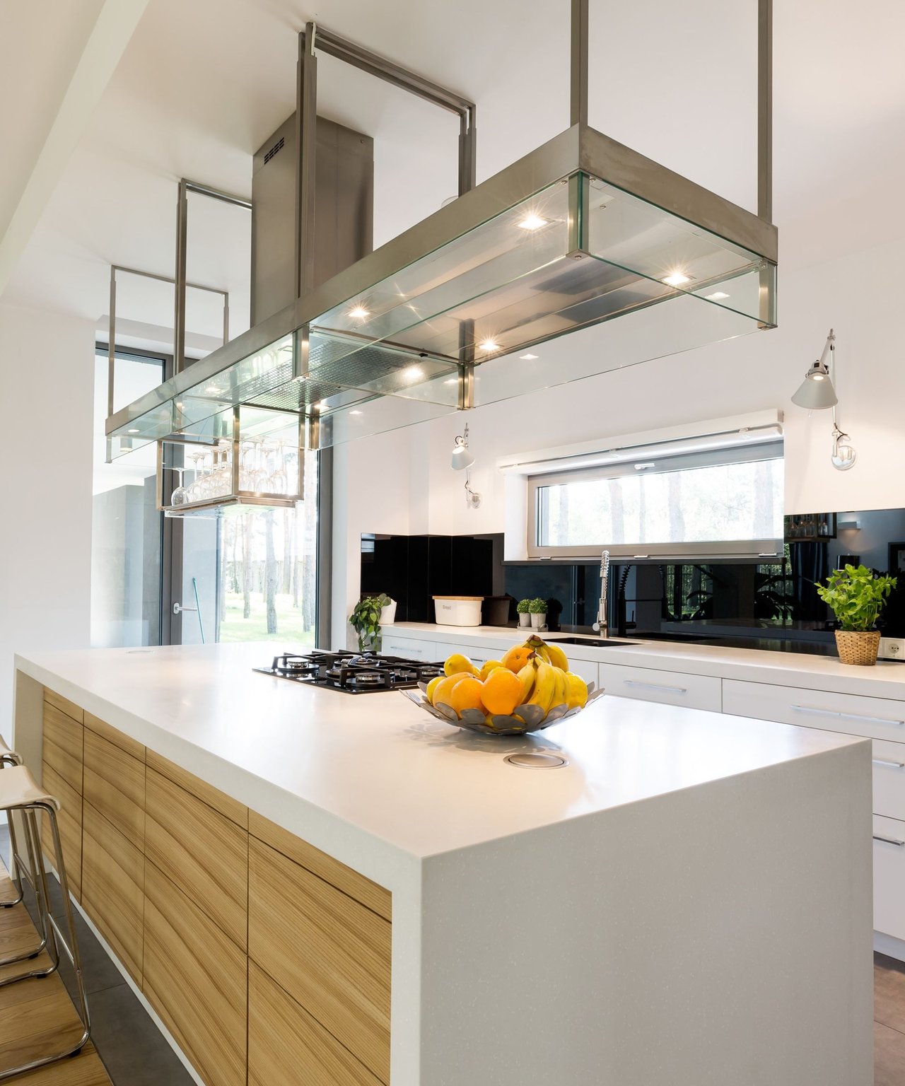 Modern kitchen with a white island, wood cabinetry, and a suspended glass range hood.