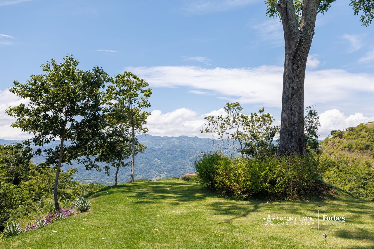 Lawn and landscaped grounds overlooking a green mountain valley beneath a bright blue sky.