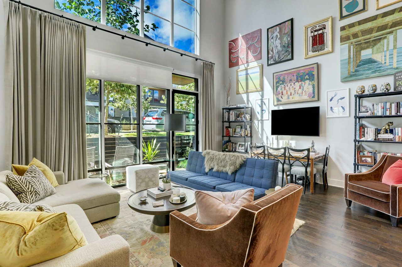 Two-story living room at The Grove townhome, Unity Circle, Austin, TX, with a wall of windows, custom draperies, a gallery wall integrating the television with framed art, and built-in shelving.