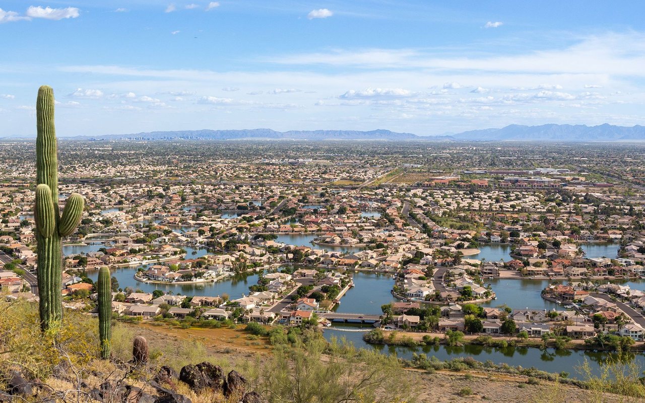 Glendale neighborhoods and lakes stretch toward distant mountains, with saguaro cacti in the foreground.