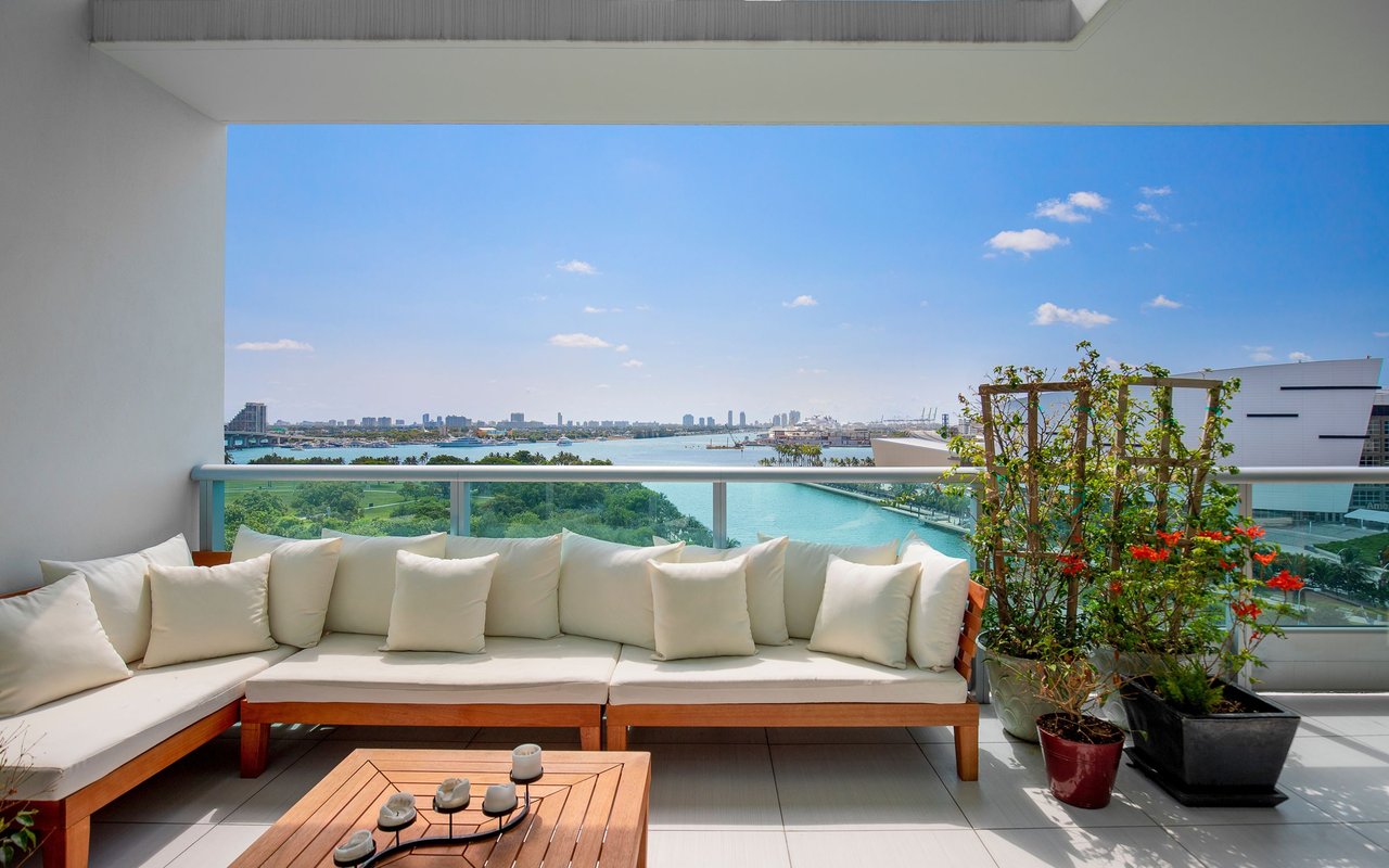 Furnished terrace with white seating and potted plants overlooking the water and city skyline.