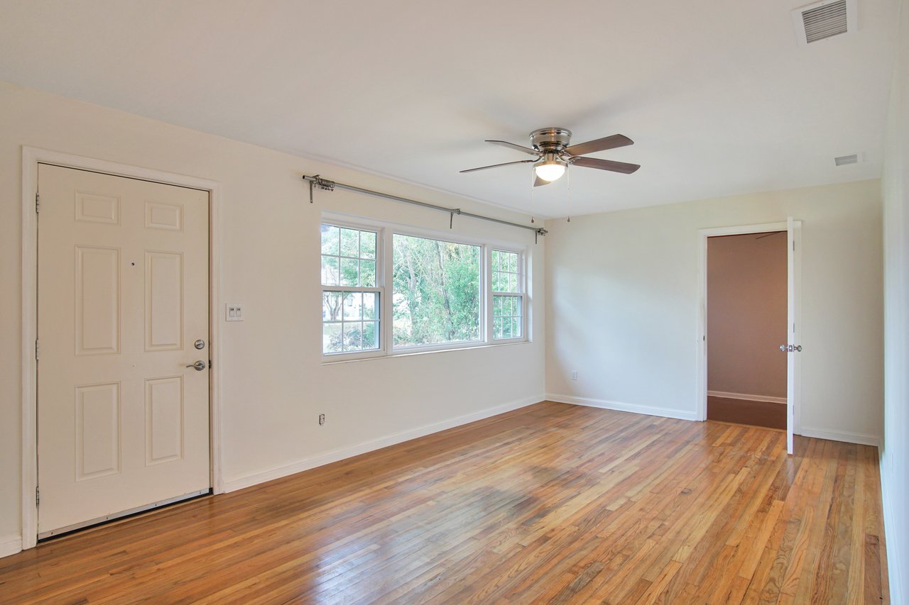 An empty room featuring hardwood floors and a ceiling fan, creating a spacious and airy atmosphere.