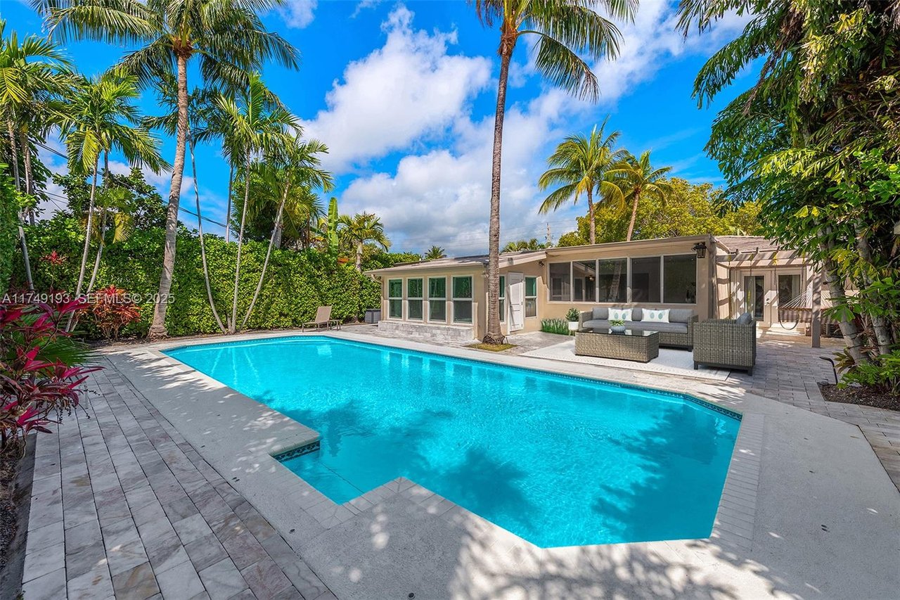 Backyard pool beside a single-story home, with palm trees and a paved patio.