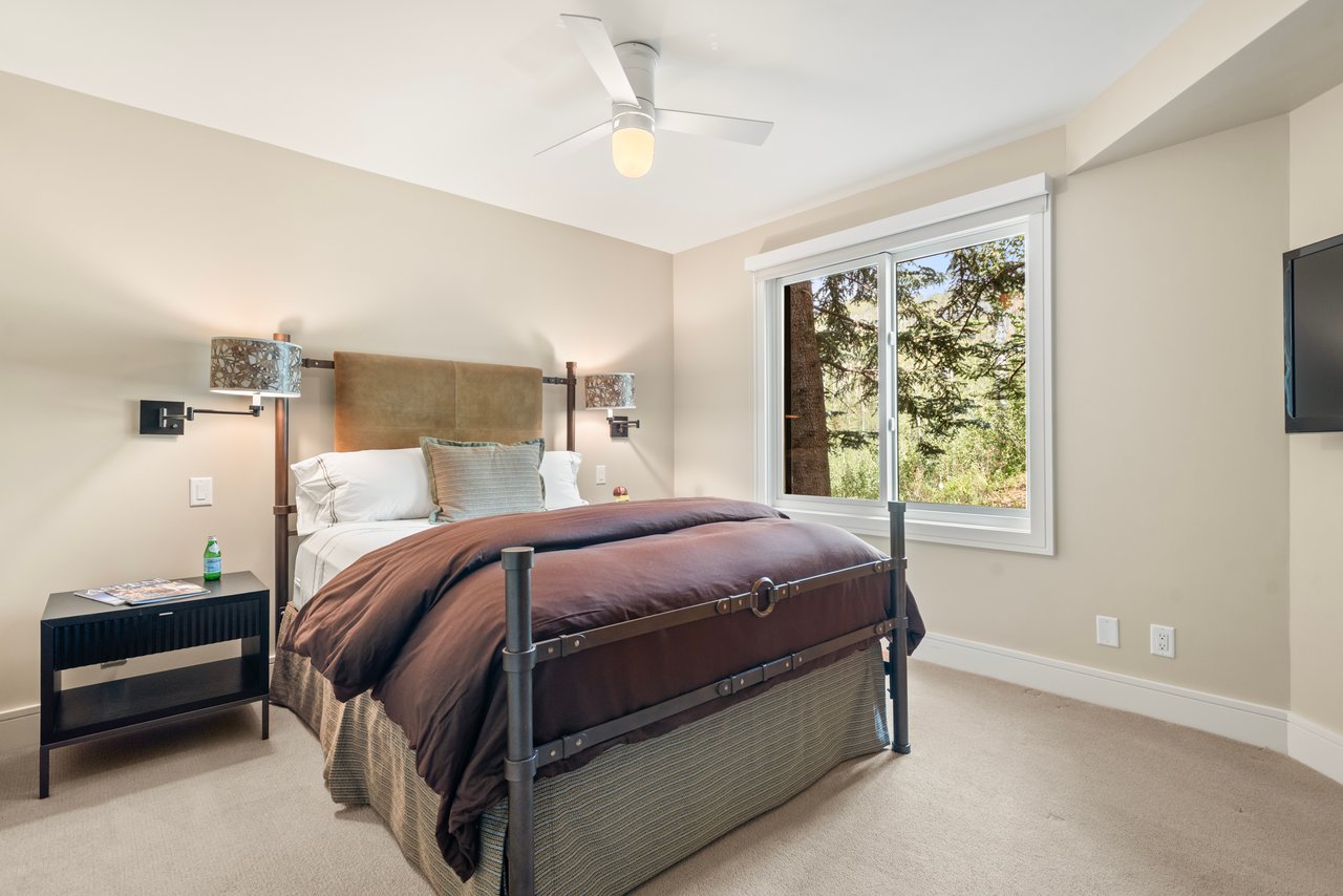 Bedroom with a metal-frame bed and large window overlooking trees.