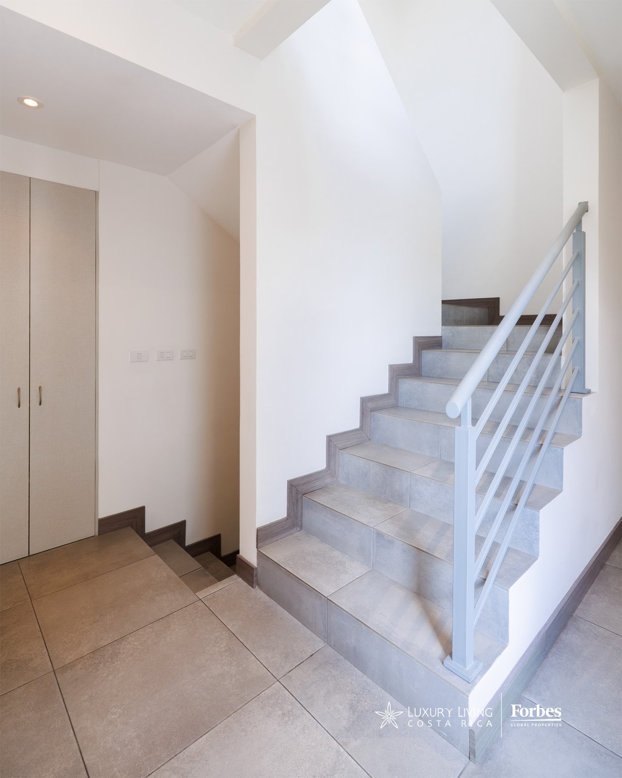 Tiled townhouse staircase with a pale railing, high ceiling, and built-in closet.