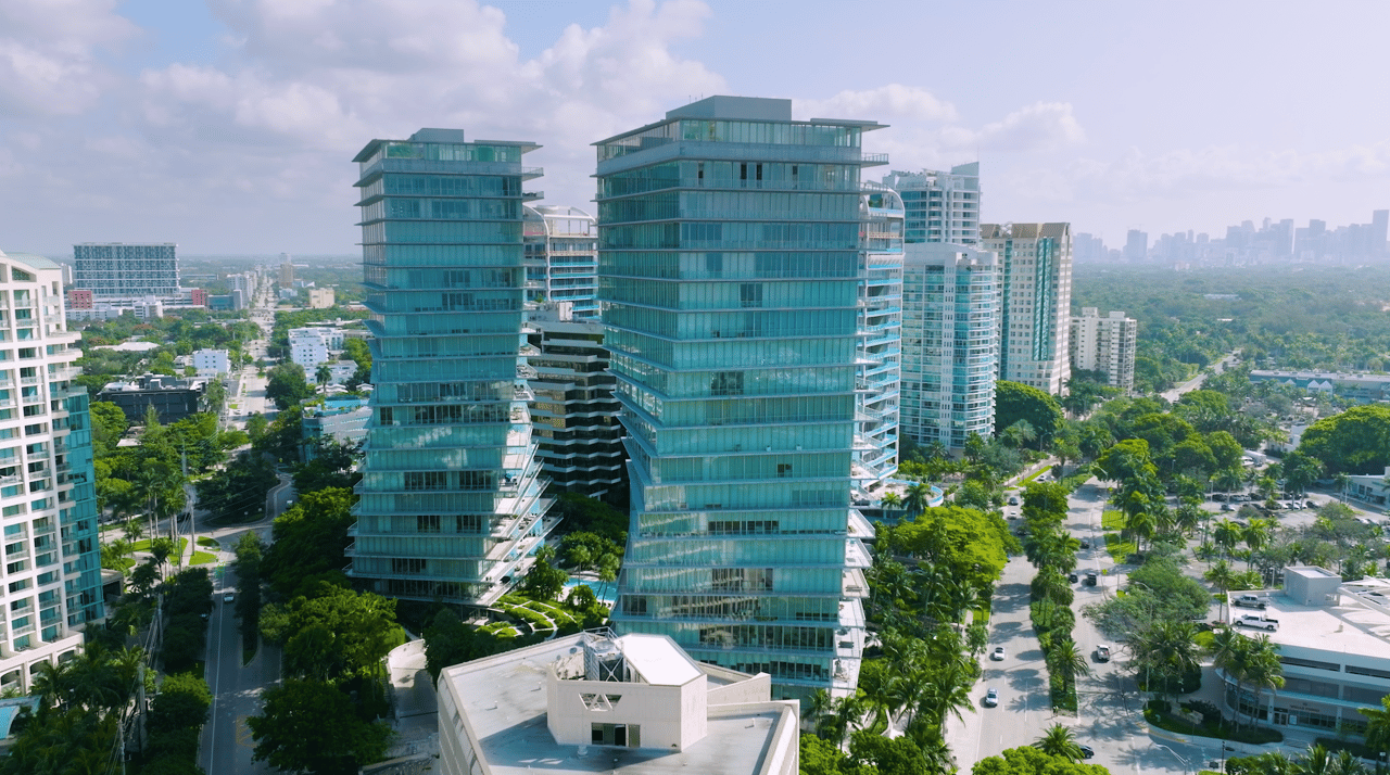 Aerial view of glass condominium towers rising above Coconut Grove's leafy streets.