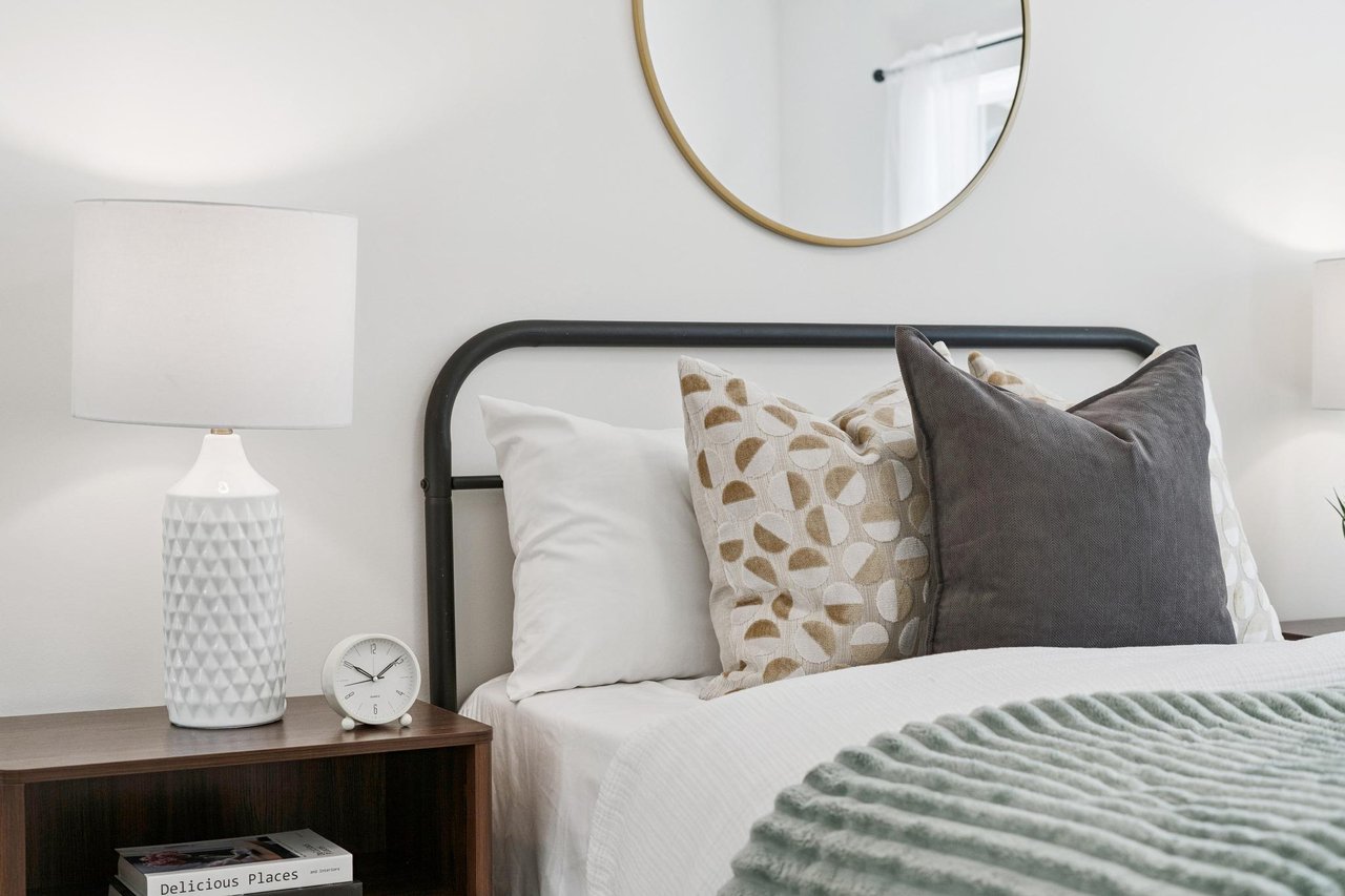 Bedroom with a black metal headboard, layered pillows, and a dark wood bedside table.