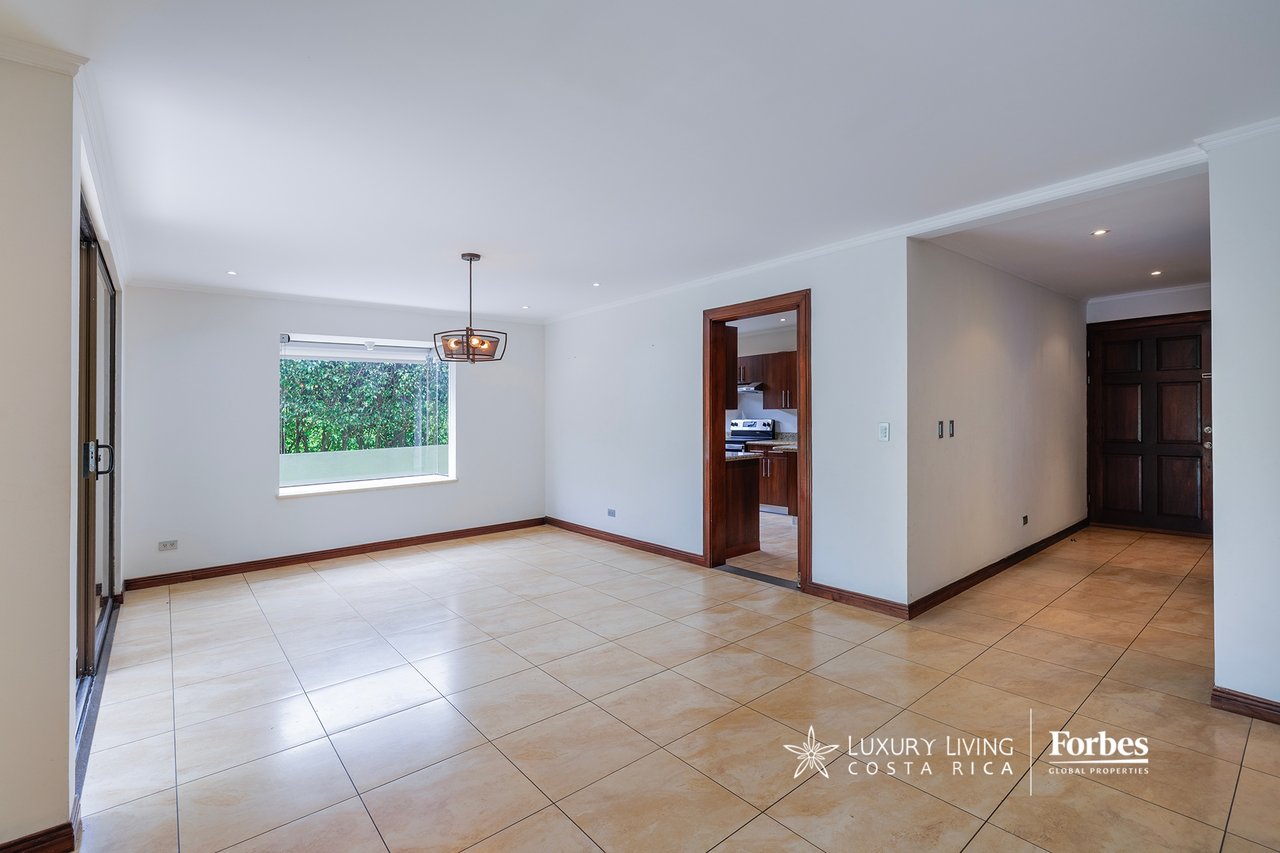 Unfurnished living and dining area with pale tile floors, a greenery-facing window, and a doorway to the kitchen.