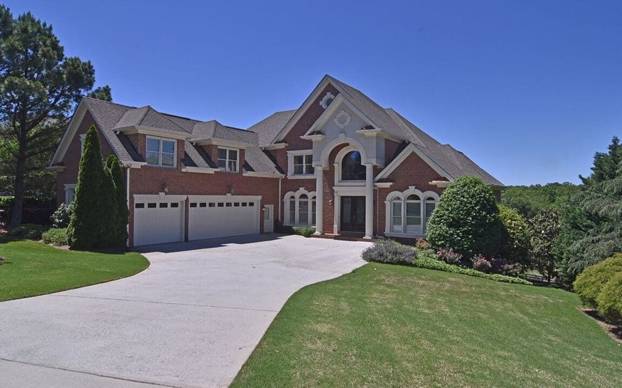 Two-story brick house with an arched entrance, double garage, curved driveway, and manicured lawn.