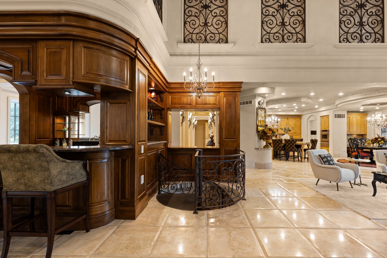 Luxury kitchen with dark wood cabinetry, curved breakfast bar, wrought-iron details, and chandelier.