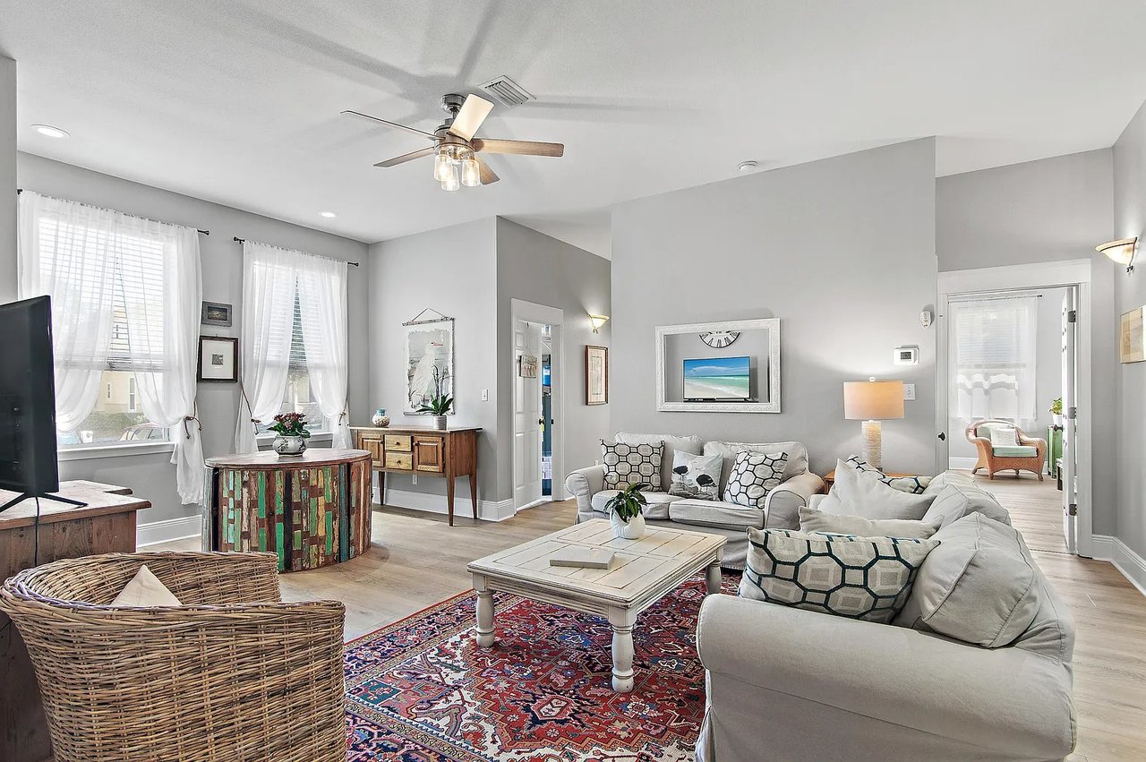 Living room with white sofas, a colorful patterned rug, and two large curtained windows.