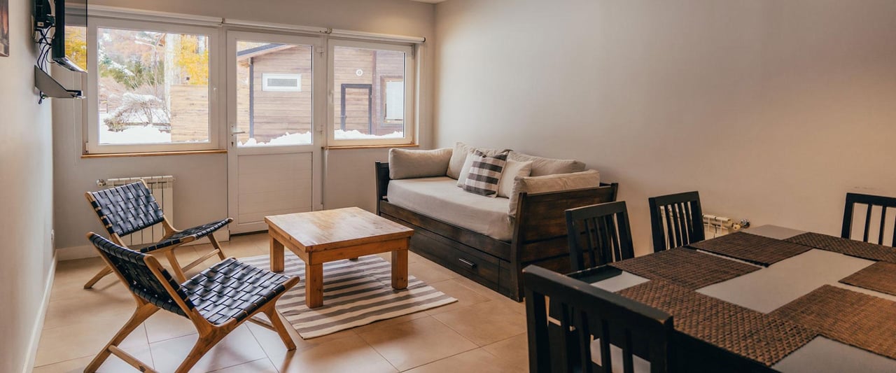 Living and dining area with woven chairs and snowy views through the windows.
