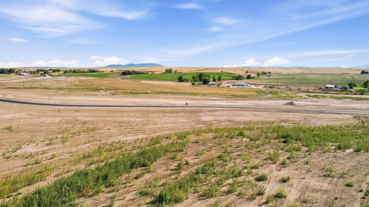 Graded development lots and a paved road across open rural land, with fields and low hills in the distance.