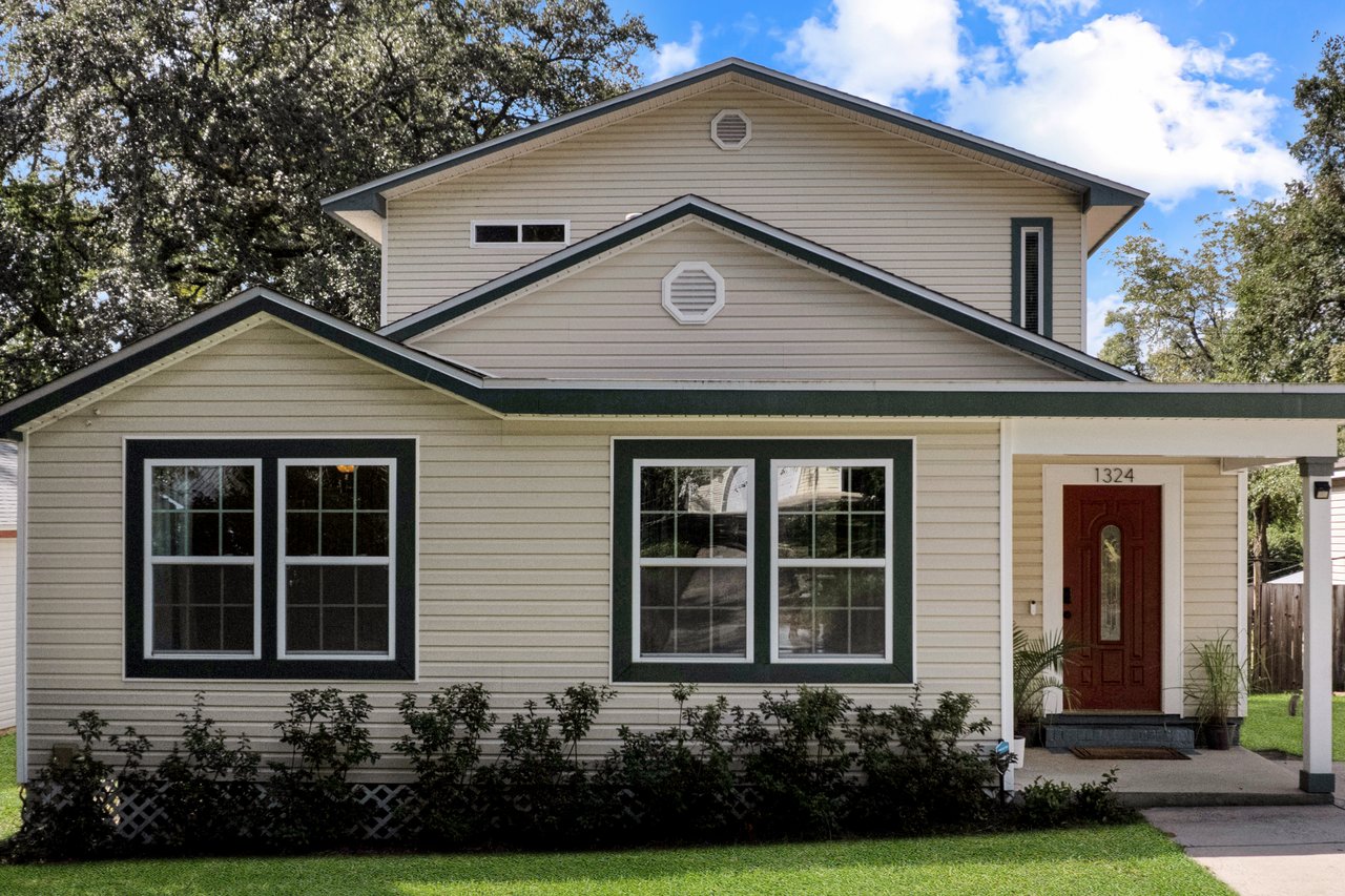 Small cream-colored house with green trim, a red door, and a porch. Surrounded by green grass and shrubs, evoking a welcoming and cozy feel at 1324 Branch Street in Tallahassee, Florida.