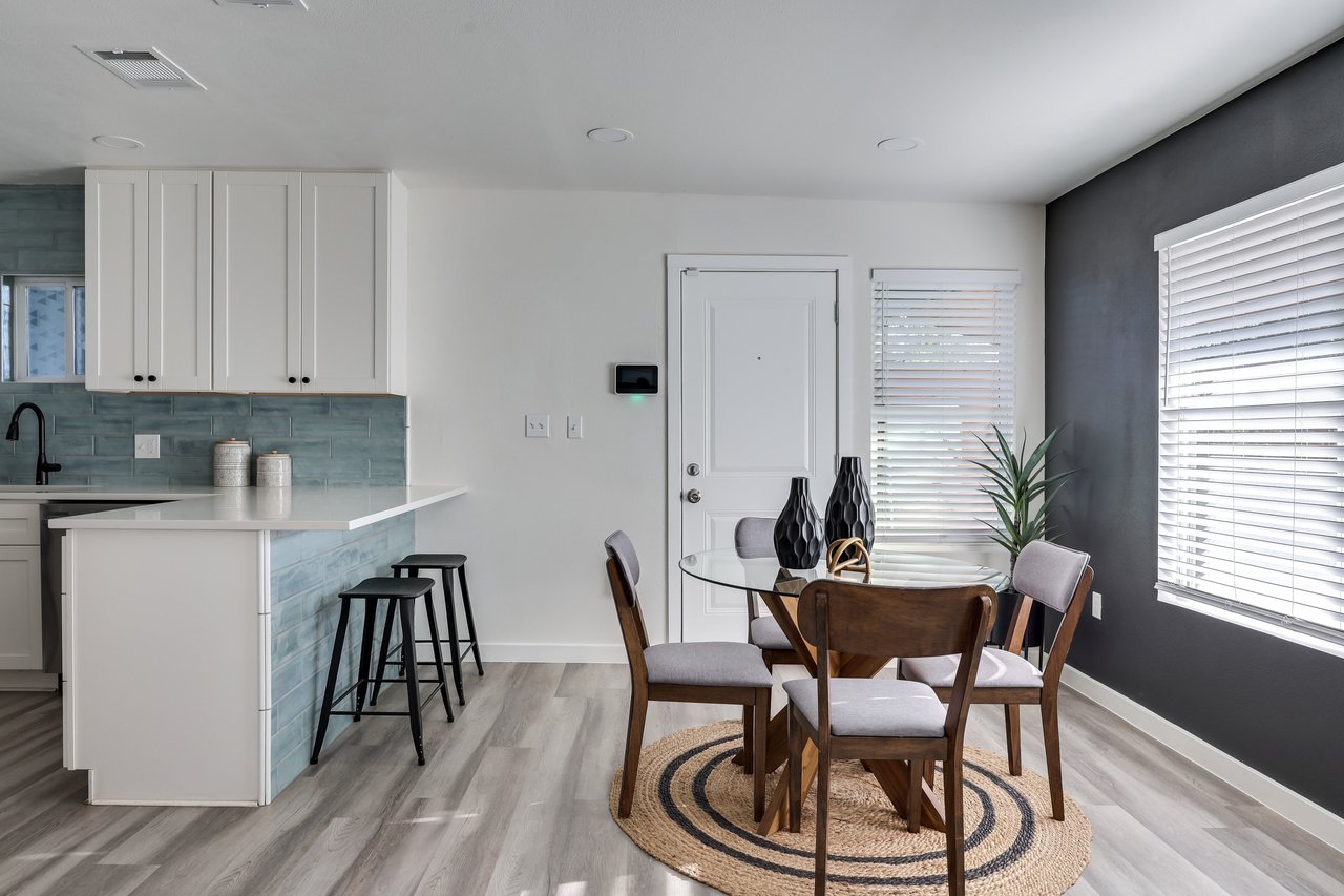 Open-plan kitchen and dining area with blue tile backsplash, peninsula seating, and a round glass table.