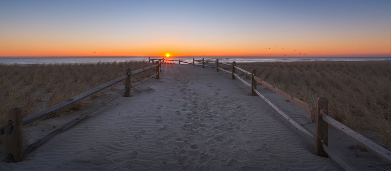 Boardwalk through Strathmere dunes leading to the ocean at sunset.
