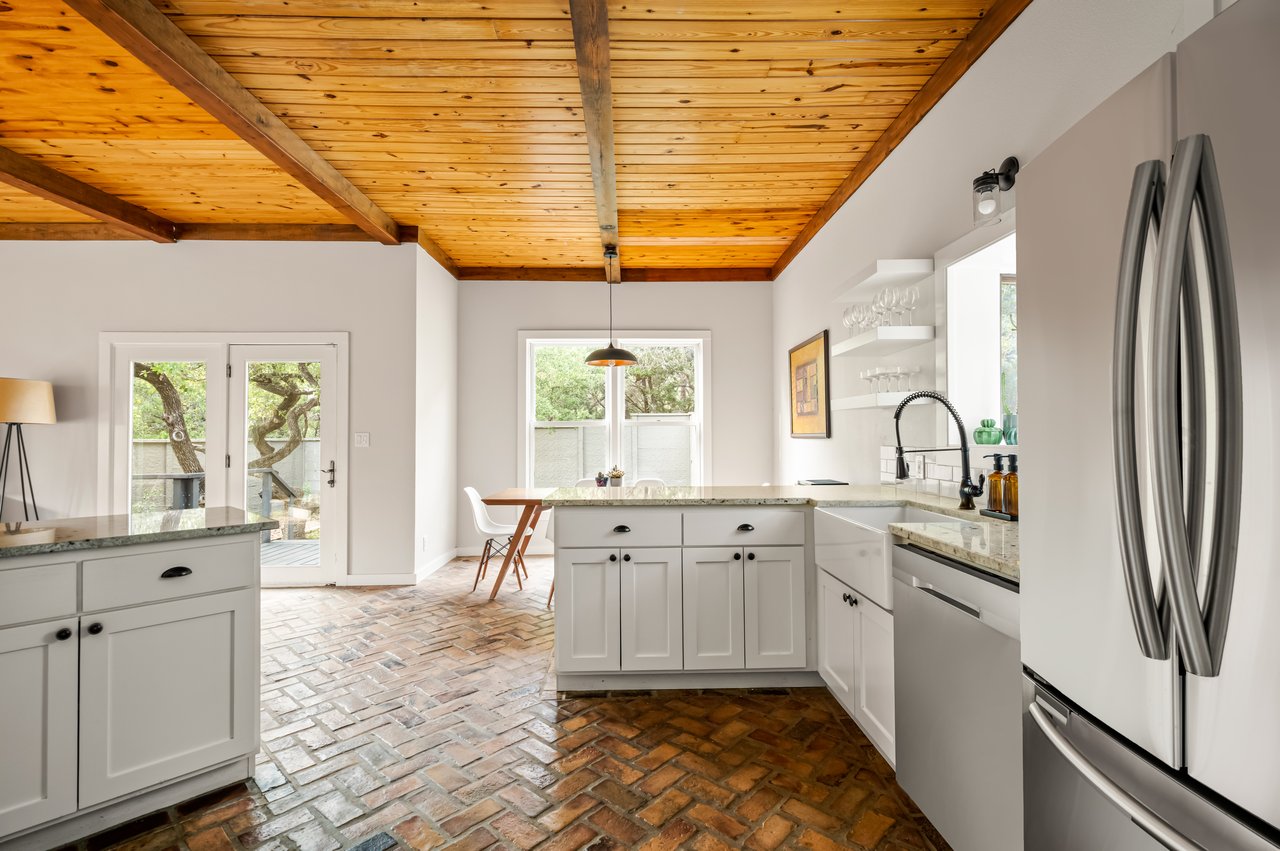 Bright kitchen with exposed timber ceiling, brick flooring, white island, and stainless steel appliances.