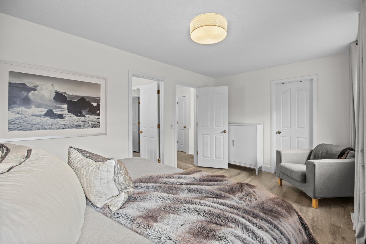 Bedroom with a gray faux-fur bed throw, framed ocean-wave photograph, and gray armchair.