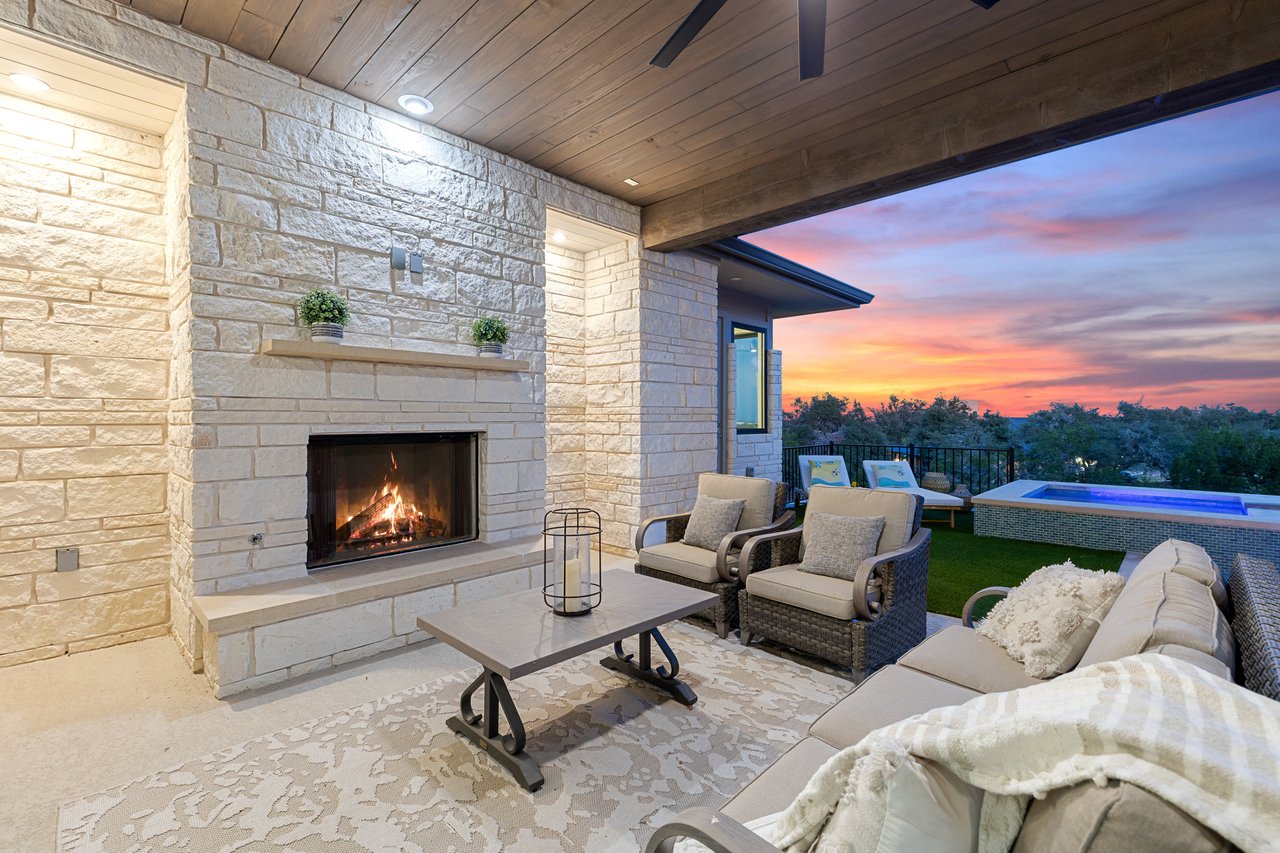 Covered patio with an outdoor stone fireplace and pool view at sunset, at this Bee Caves home on Caudill Lane, Austin, Texas.