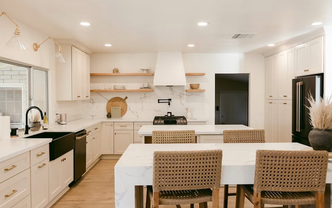 Bright white kitchen with marble-patterned counters, brass hardware, black appliances, and a large island.
