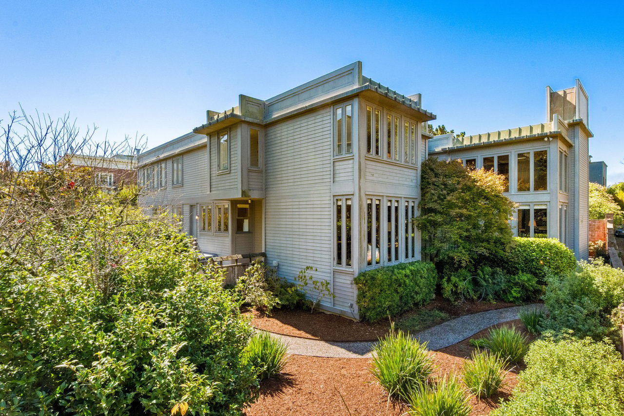 Modern two-story home with tall windows, landscaped gardens, and a curved path.