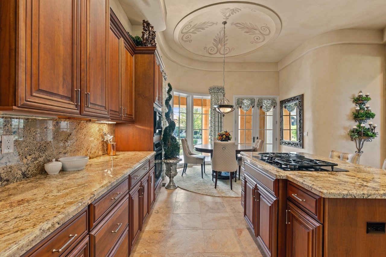 Kitchen with cherry cabinetry, stone counters, a gas cooktop island, and an adjoining dining area.