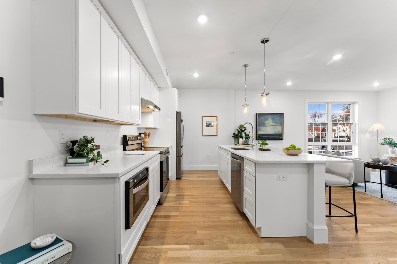 Bright modern kitchen with white cabinetry, stainless appliances, and a large island overlooking the living area.