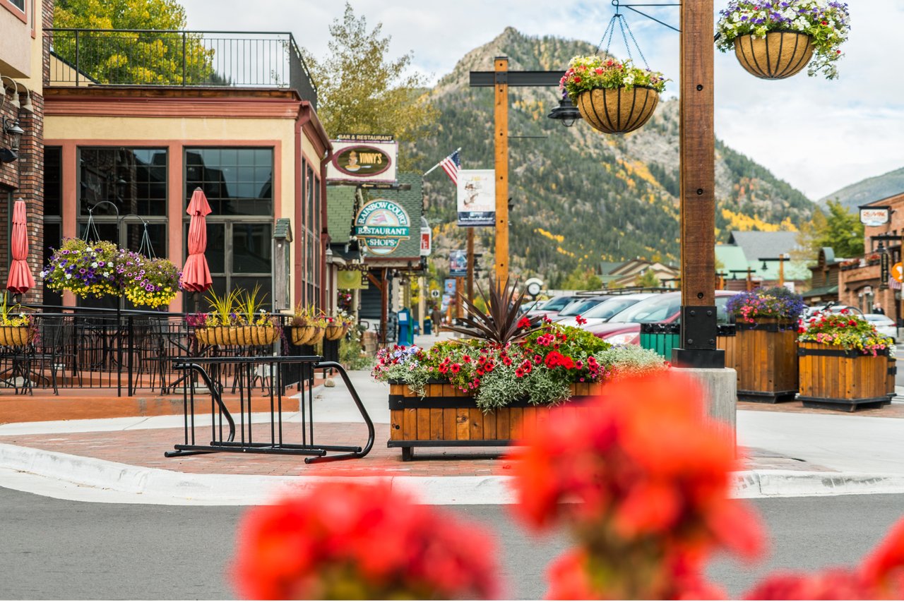 Downtown Frisco street with flower planters, storefronts, outdoor dining, and autumn-colored mountain slopes.