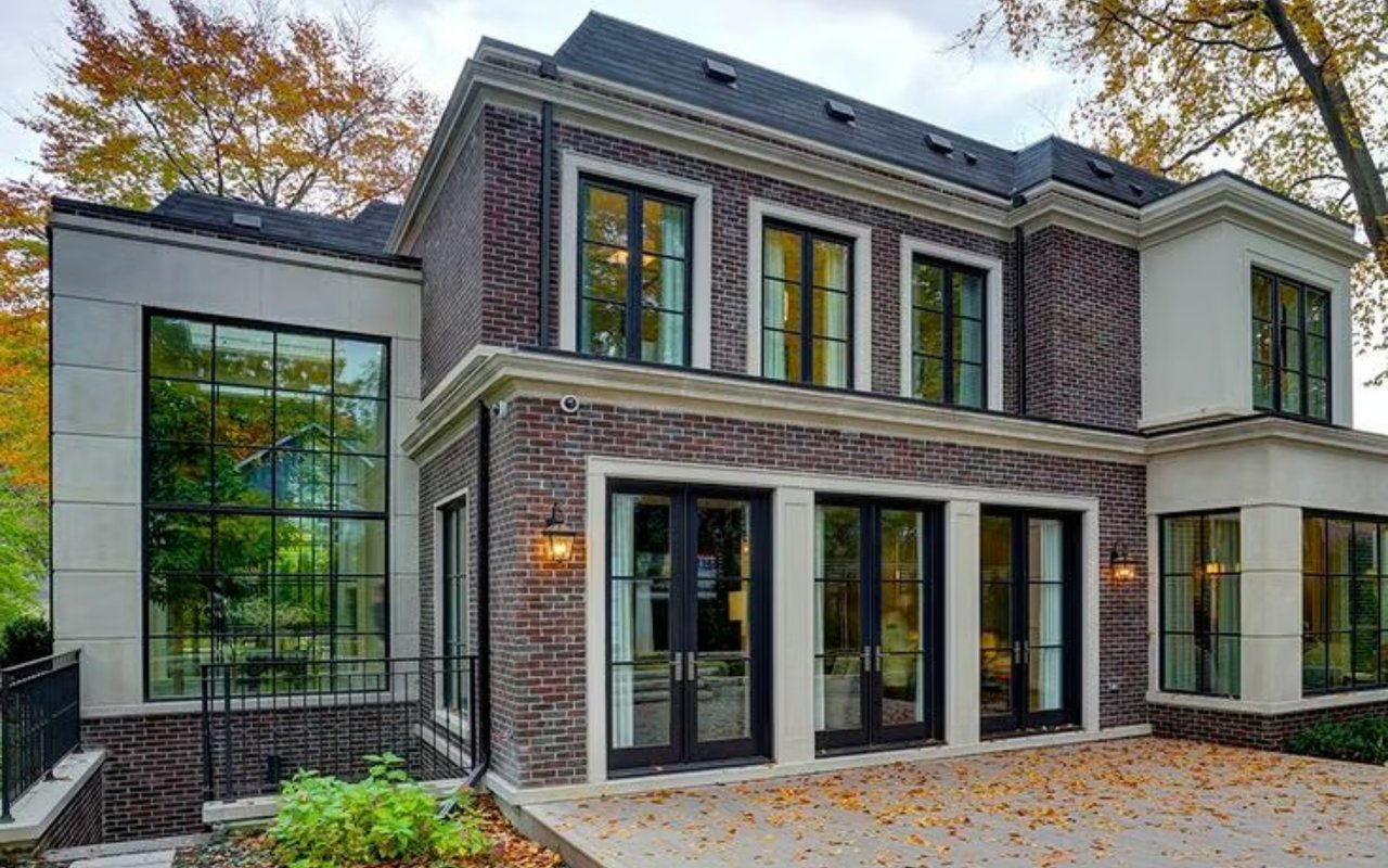 Modern brick-and-stone home with large windows and a leaf-strewn patio