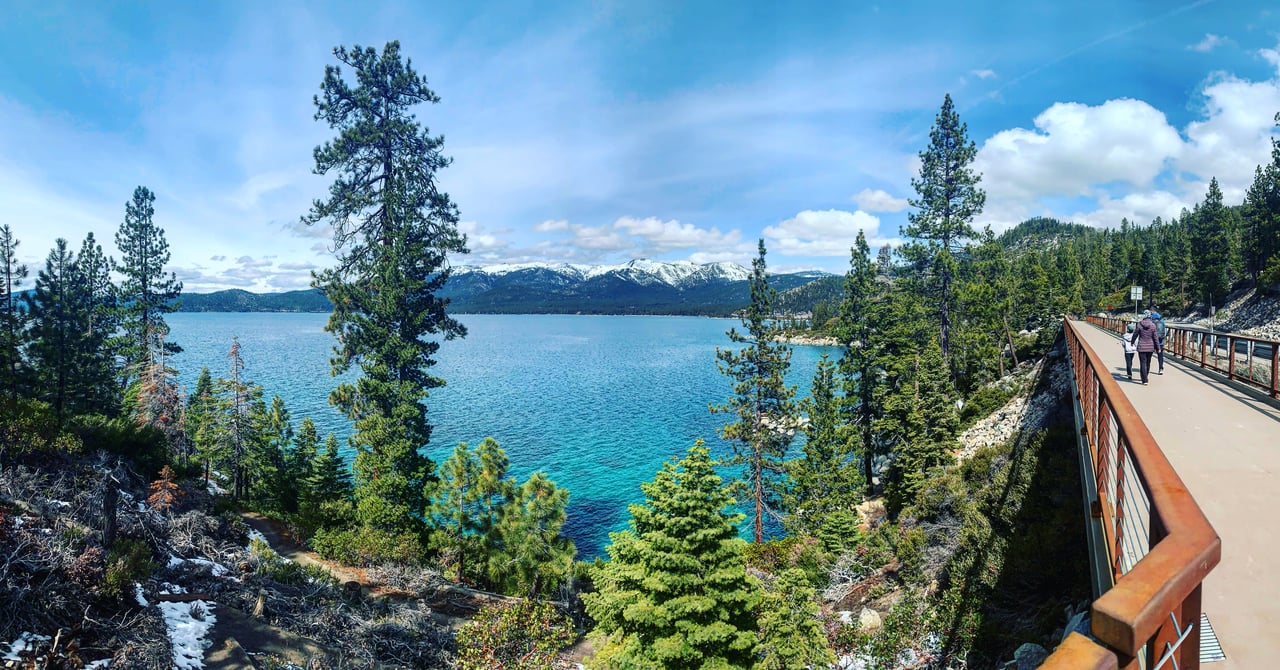 A stunning aerial view of Incline Village, Nevada, showcasing luxury homes, Lake Tahoe's crystal-clear waters, and the surrounding Sierra Nevada mountains, with neighboring towns in the distance.