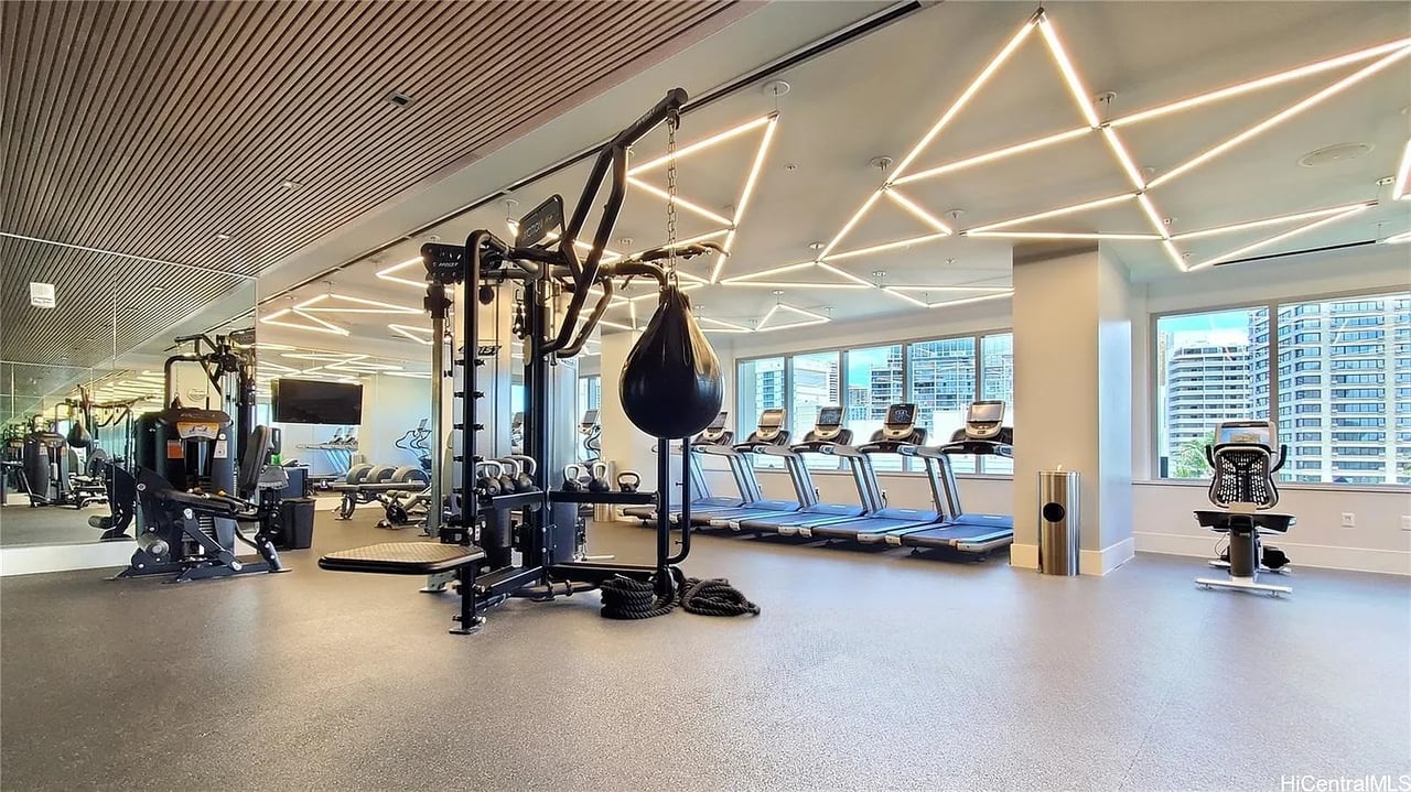 Modern fitness center with treadmills by large windows and weight-training equipment.