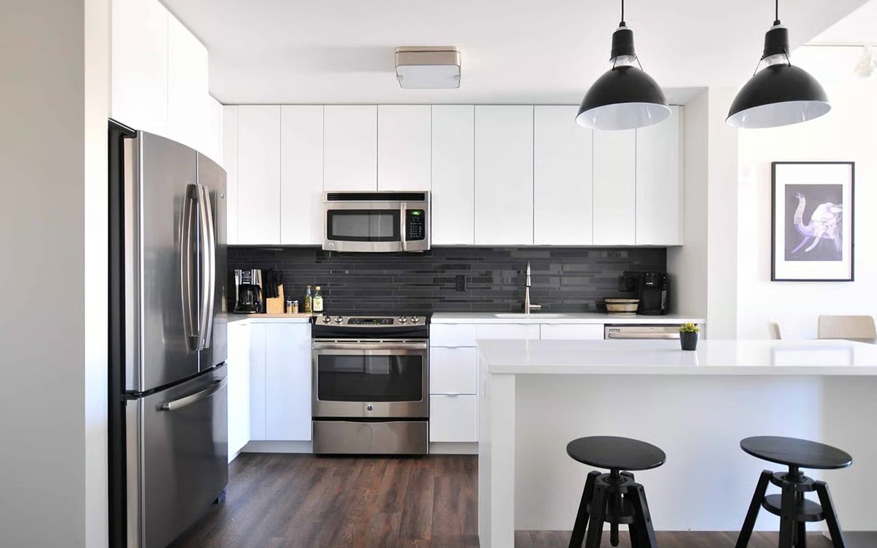 Modern white kitchen with a dark tile backsplash, stainless steel appliances, and island seating.