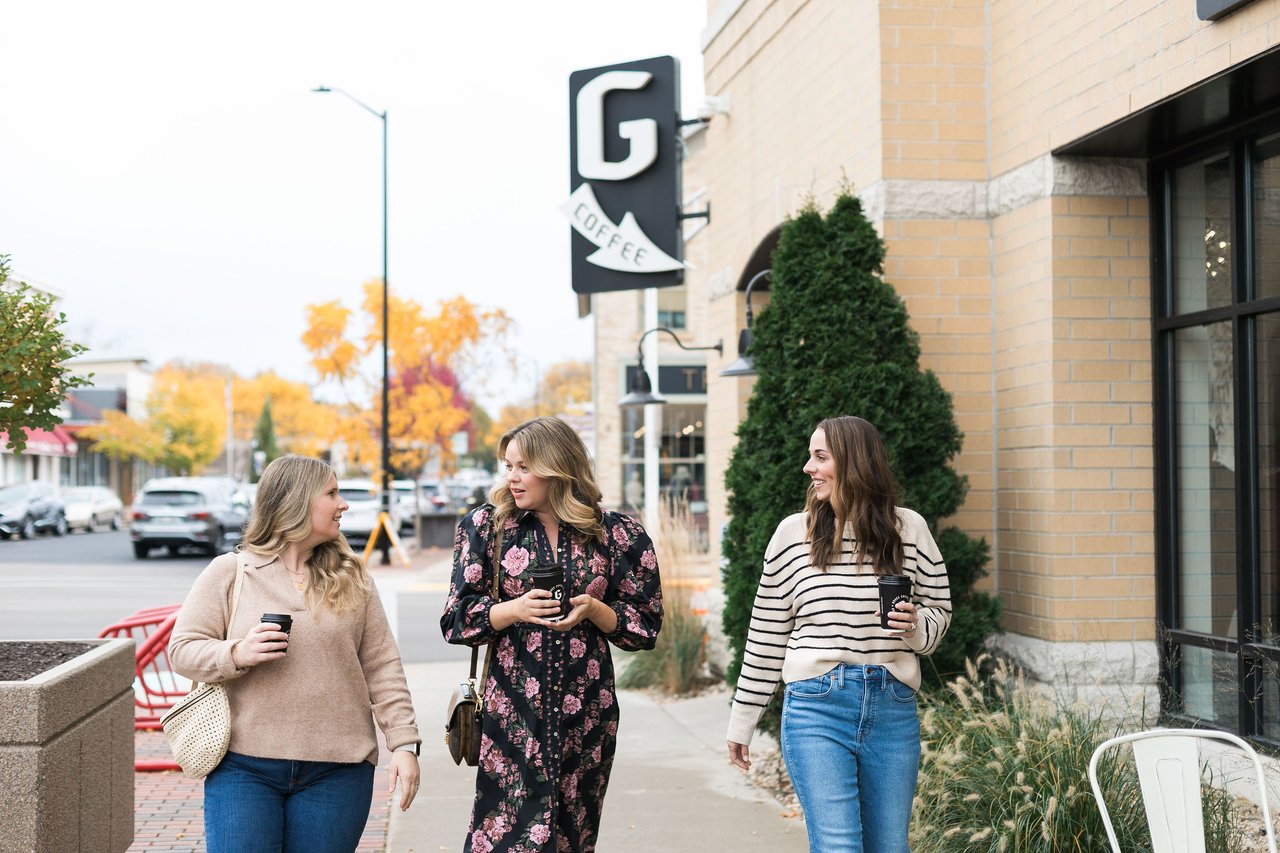 Local Madison real estate advisor Cait Berry walking and talking with clients on an autumn sidewalk with coffee representing a community focused approach to real estate.