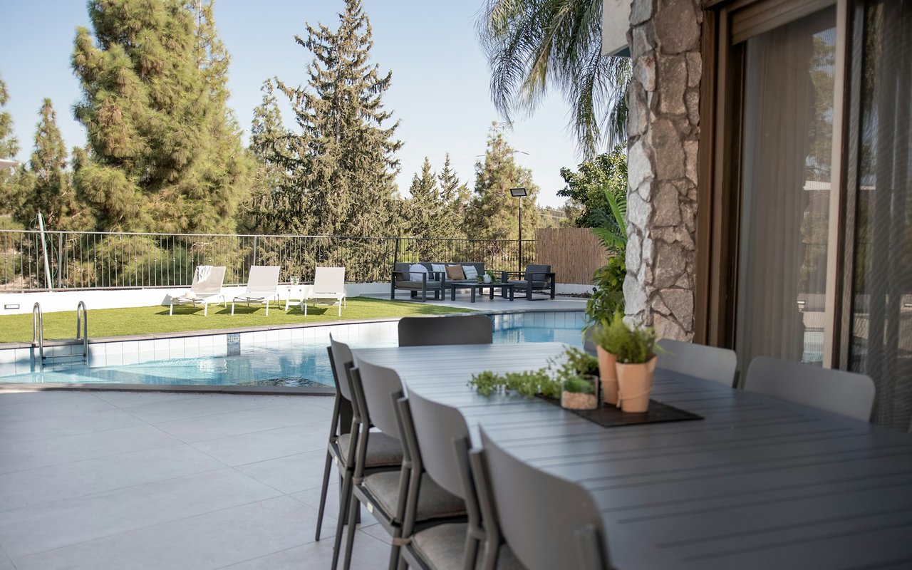 Backyard pool beside an outdoor dining patio, with loungers on a strip of green turf.