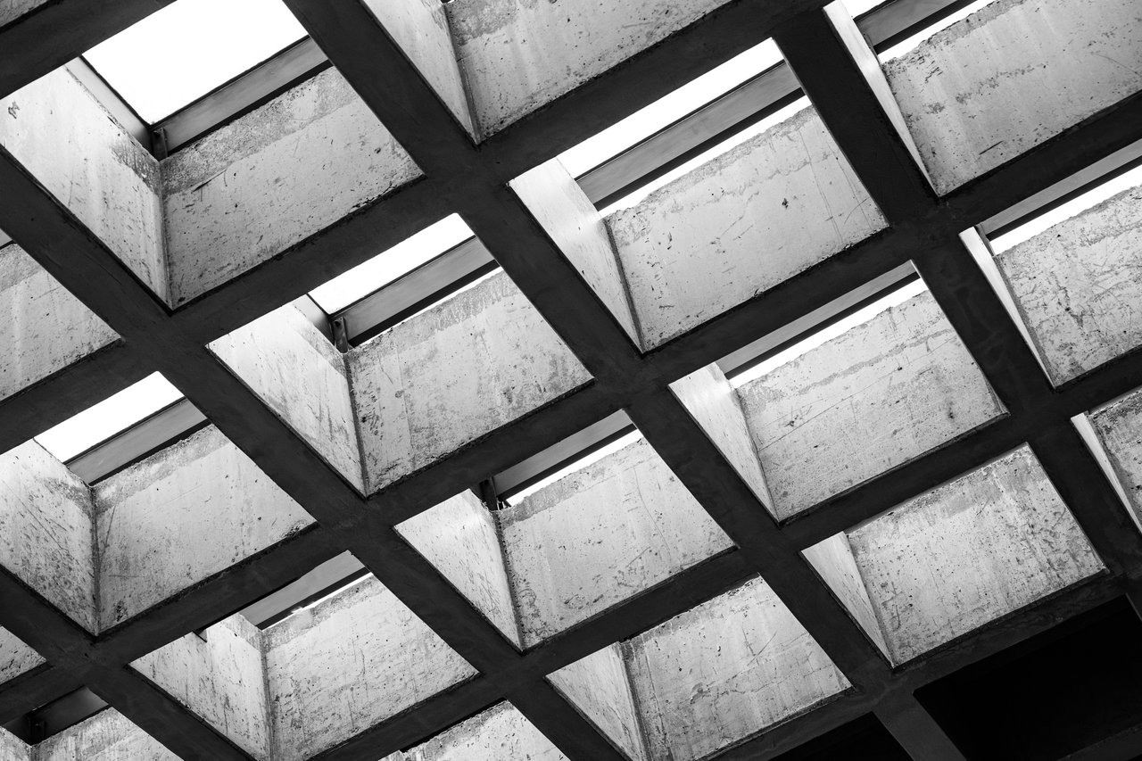 Concrete building structure with intersecting beams and rectangular openings to the sky.
