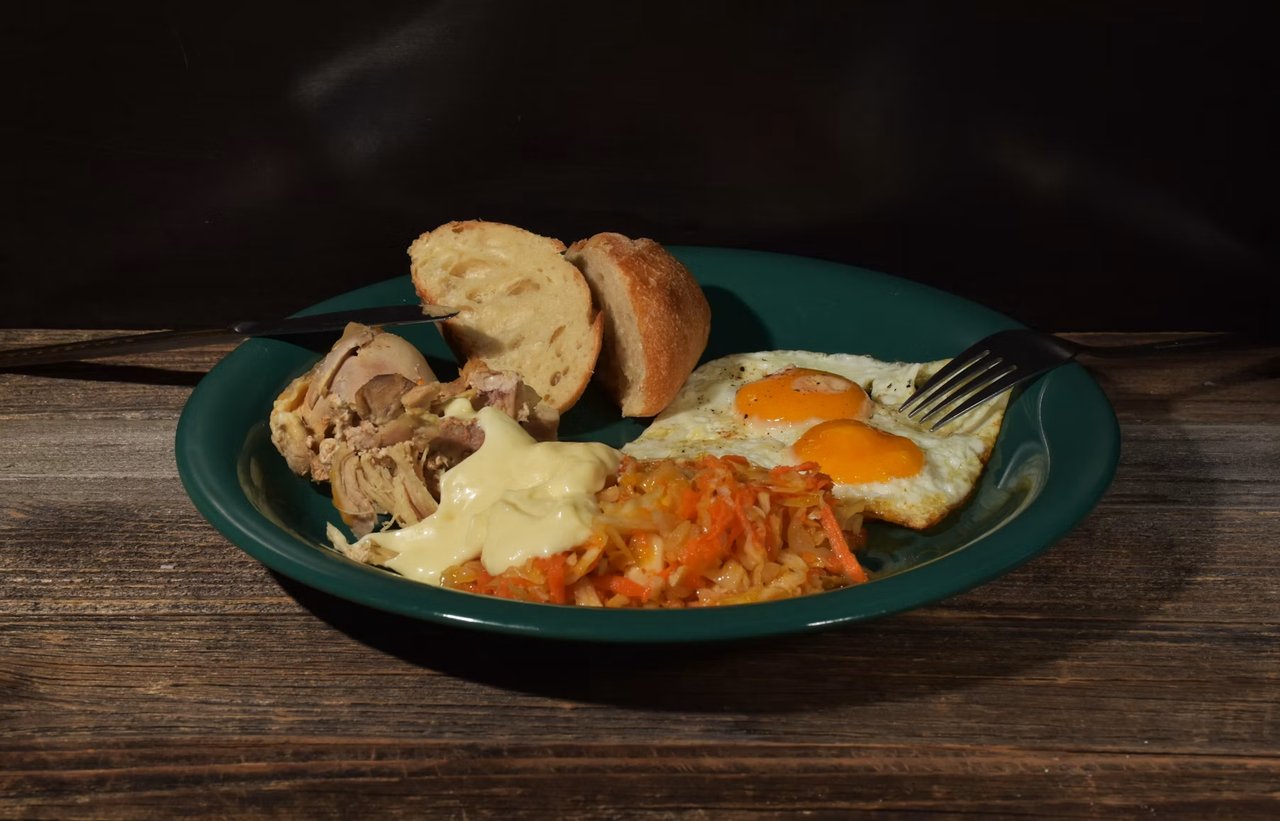 Breakfast plate with fried eggs, bread, chicken, vegetables, and melted cheese.