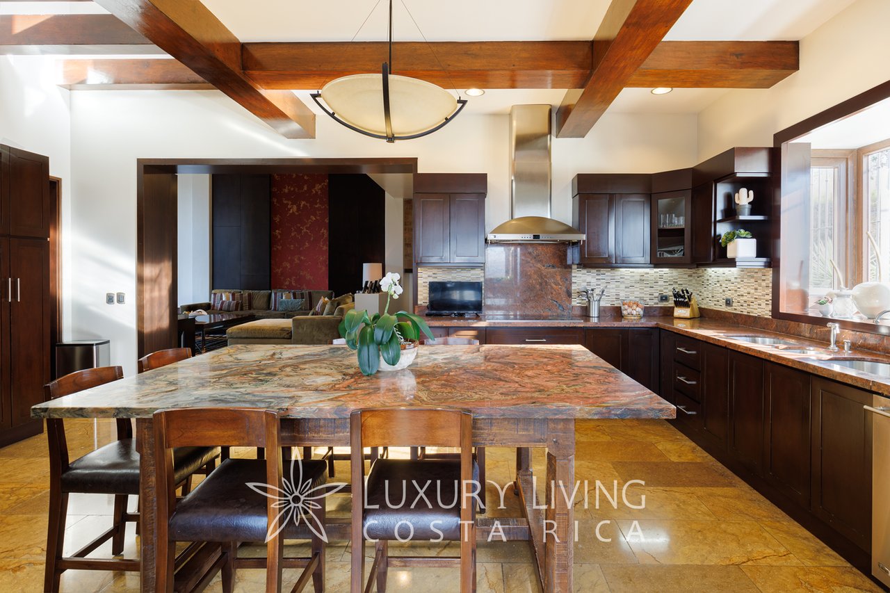 Kitchen with a large patterned stone island, dark wood cabinetry, and exposed ceiling beams.