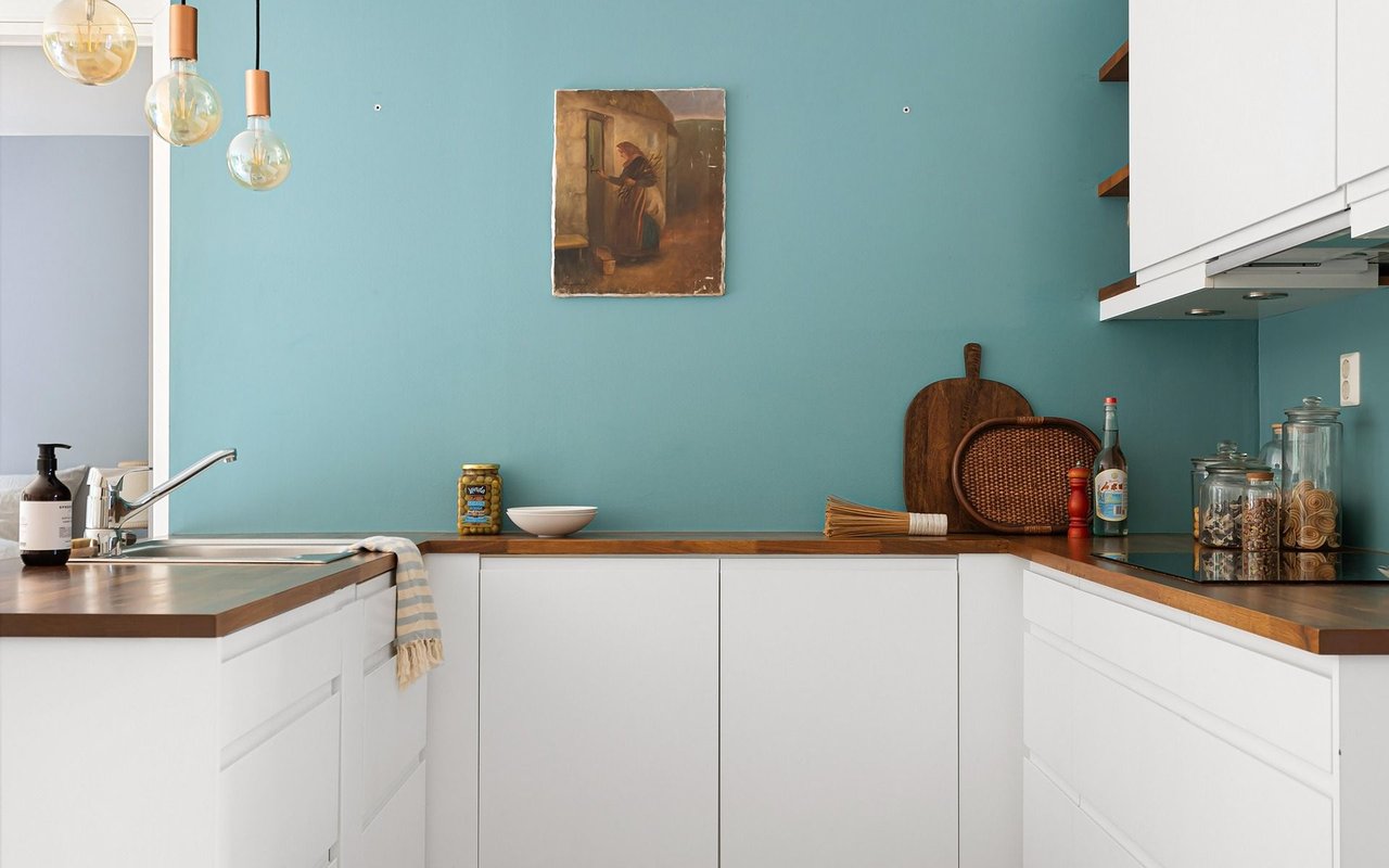 Modern kitchen with white cabinets, wood countertops, and a teal accent wall.
