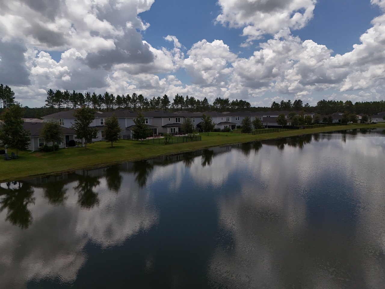 Aerial view of homes along a pond beneath a cloud-filled sky.
