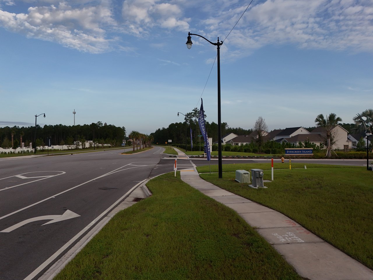 Evergreen Island neighborhood entrance with a curving road, sidewalk, streetlamps, and nearby homes.
