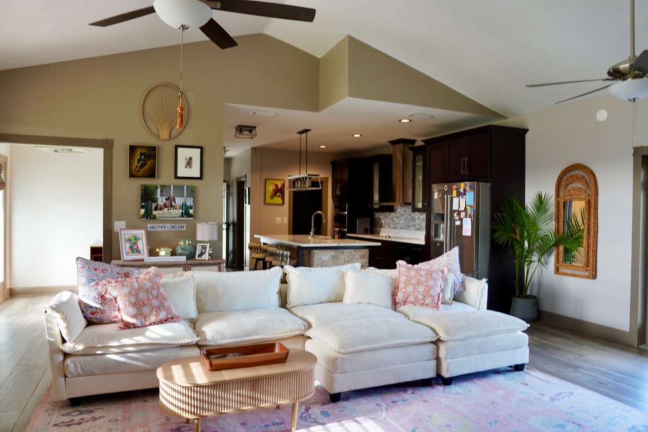 Open living room with a white sectional sofa, vaulted ceiling, and adjoining dark-cabinet kitchen.