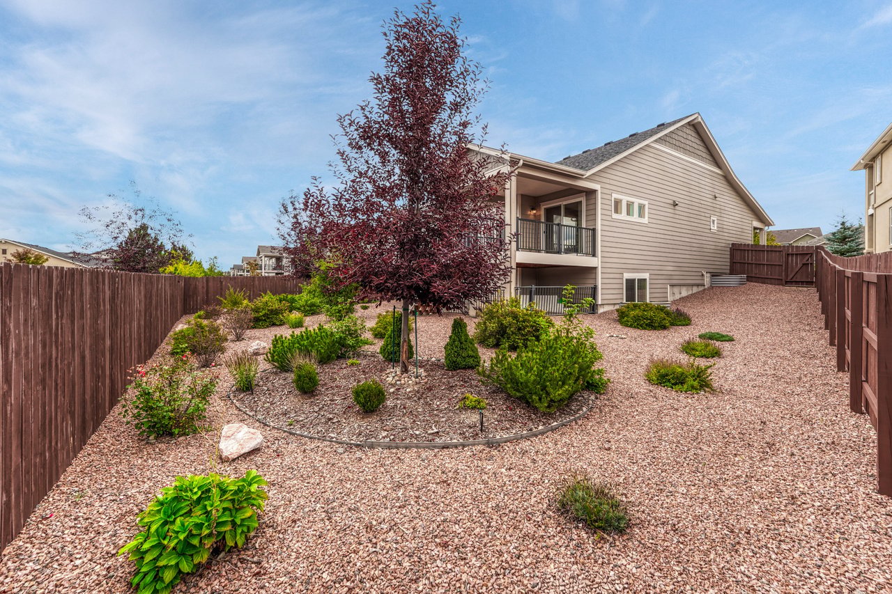 Fenced back yard with circular planting bed and gravel paths