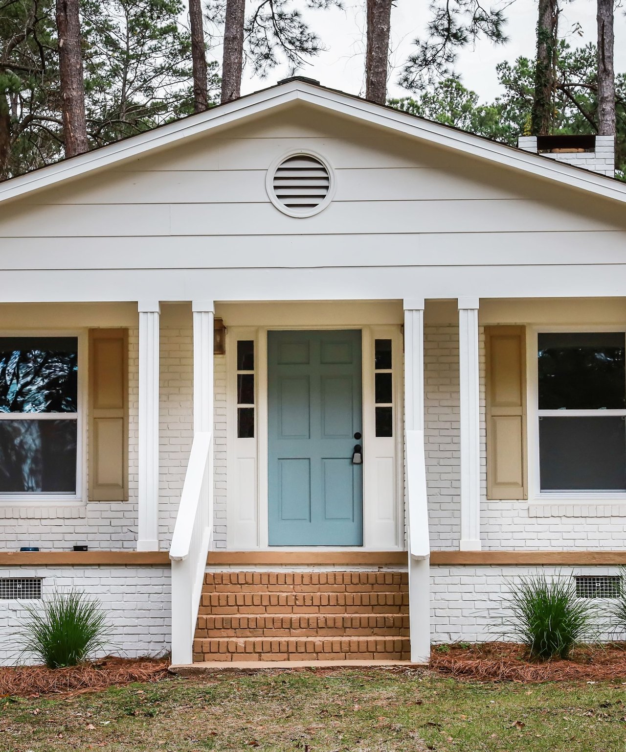 White brick house with pale blue front door, brick steps, and a circular gable vent.
