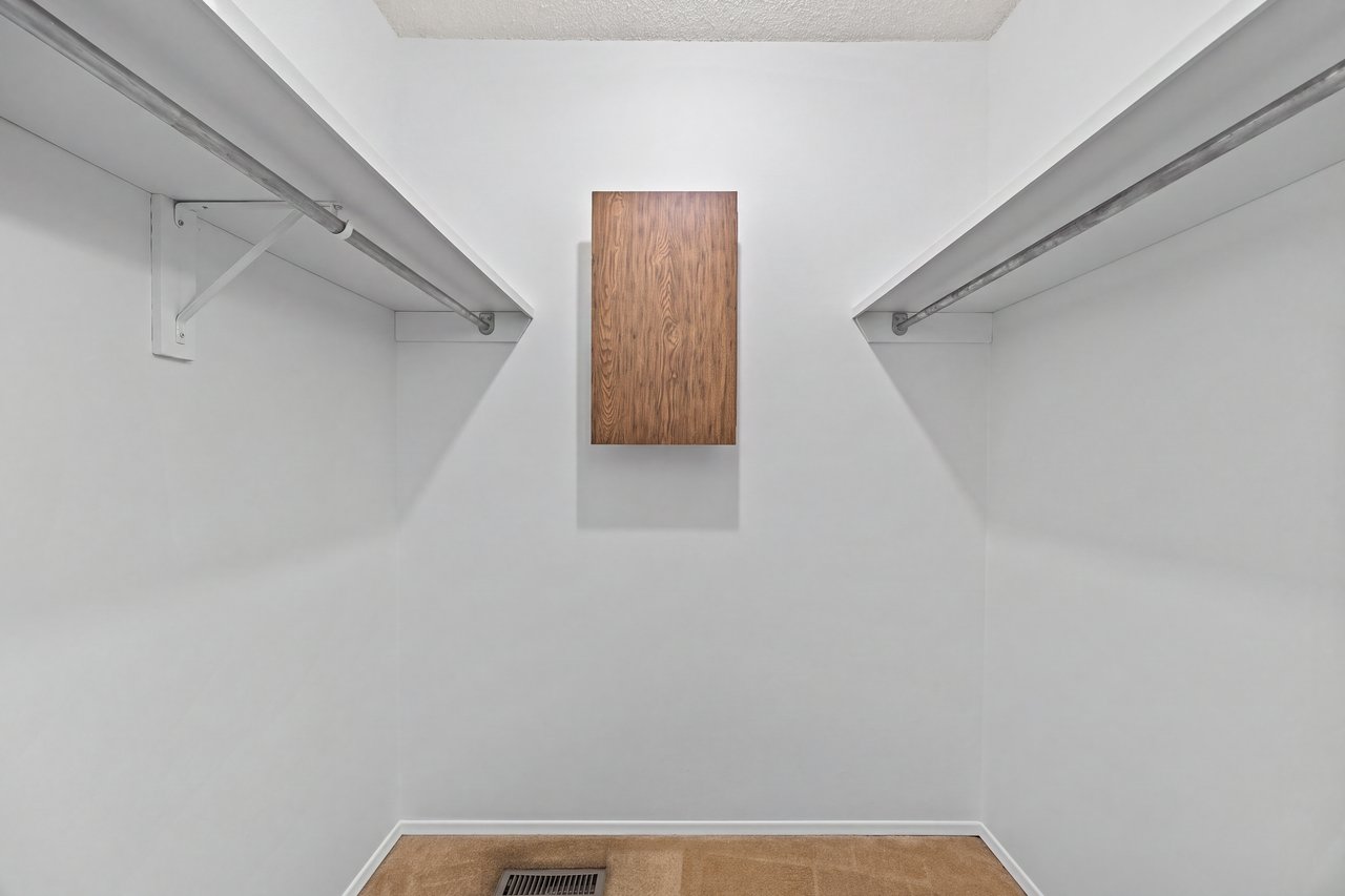 Empty walk-in closet with clothing rods on both sides and a wood-front cabinet.